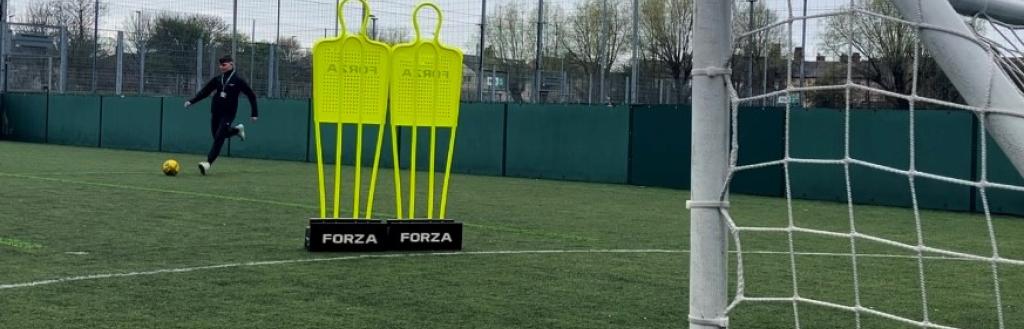 A man on an astro turf pitch kicking a football towards a net