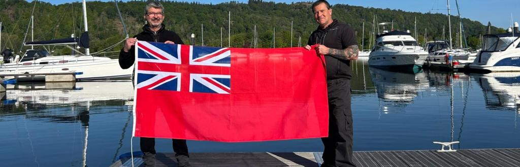 Two Lake Wardens on a jetty at Windermere, holding the Red Ensign flag.