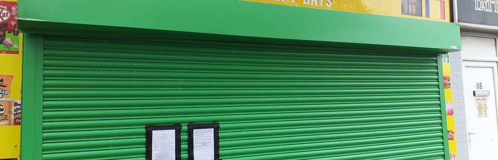 A closed shop with a green shutter. Sign reads: Easy Shop.