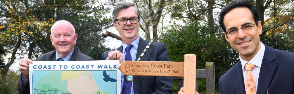 Chairs of Westmorland and Furness, North Yorkshire and Cumberland Councils holding mini Coast to Coast wooden sign and map