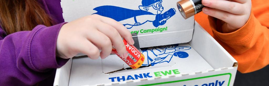 Two schoolchildren placing used batteries in a collection box