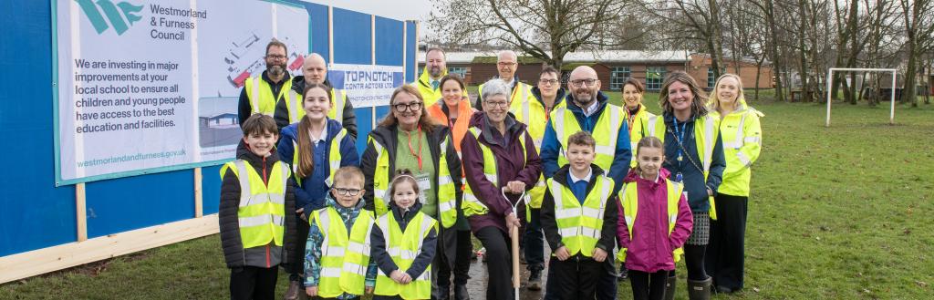 Stakeholders and children at Besconside School with a spade in the ground