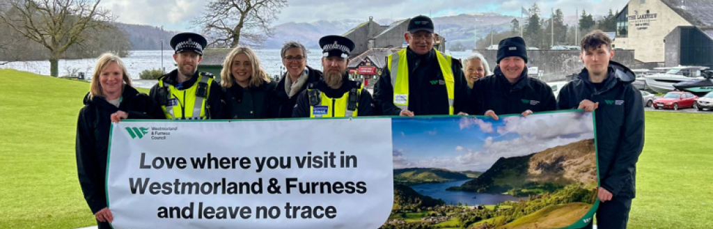 Westmorland and Furness Council and Cumbria Police officers stood holding a banner which reads "Love where you visit and leave no trace" with a mountainous landscape in the background