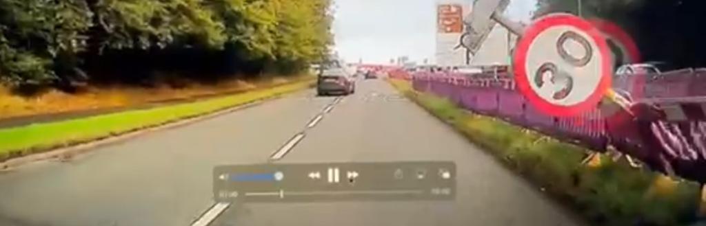 A sign falling into a road, viewed through a car windscreen.